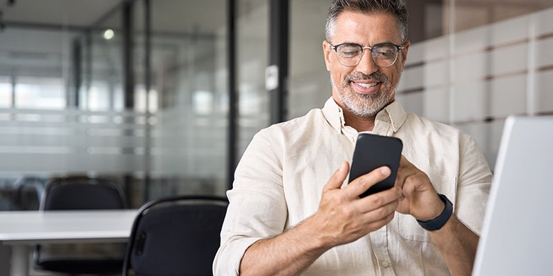 A person is seated at a desk, holding a smartphone and looking at the screen